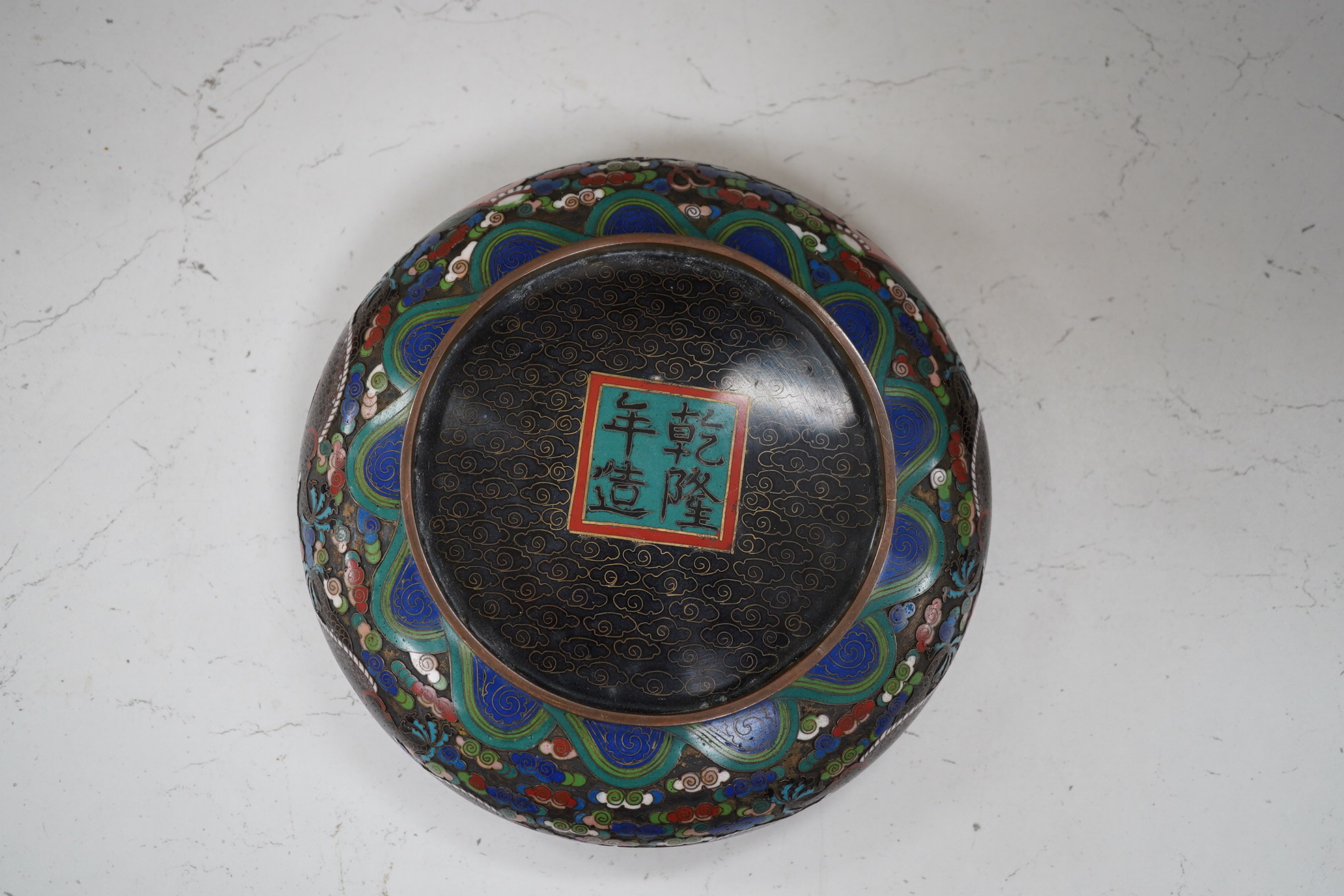 A Chinese cloisonné enamel ‘dragon’ bowl, Qianlong mark but early 20th century, on hardwood stand, 20cm diameter. Condition - poor to fair